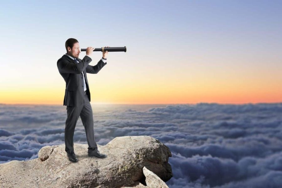 Side view of attractive young caucasian businessman standing on cliff and looking into the distance on bright blue sky and clouds background with mock up place for your advertisement. Market research, exploration and future concept